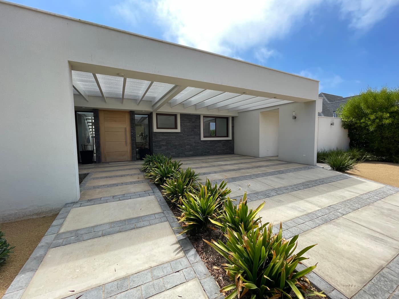 Acceso de casa moderna con pérgola y pavimentos de piedra